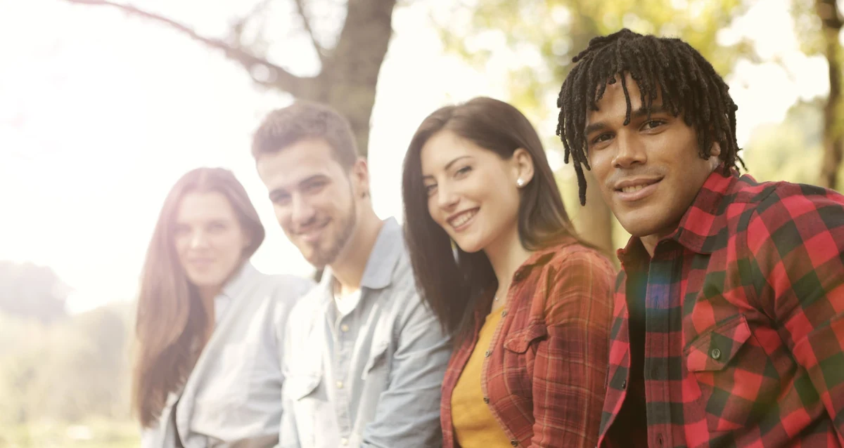 Four friends sit together outdoors and smile in warm sunlight